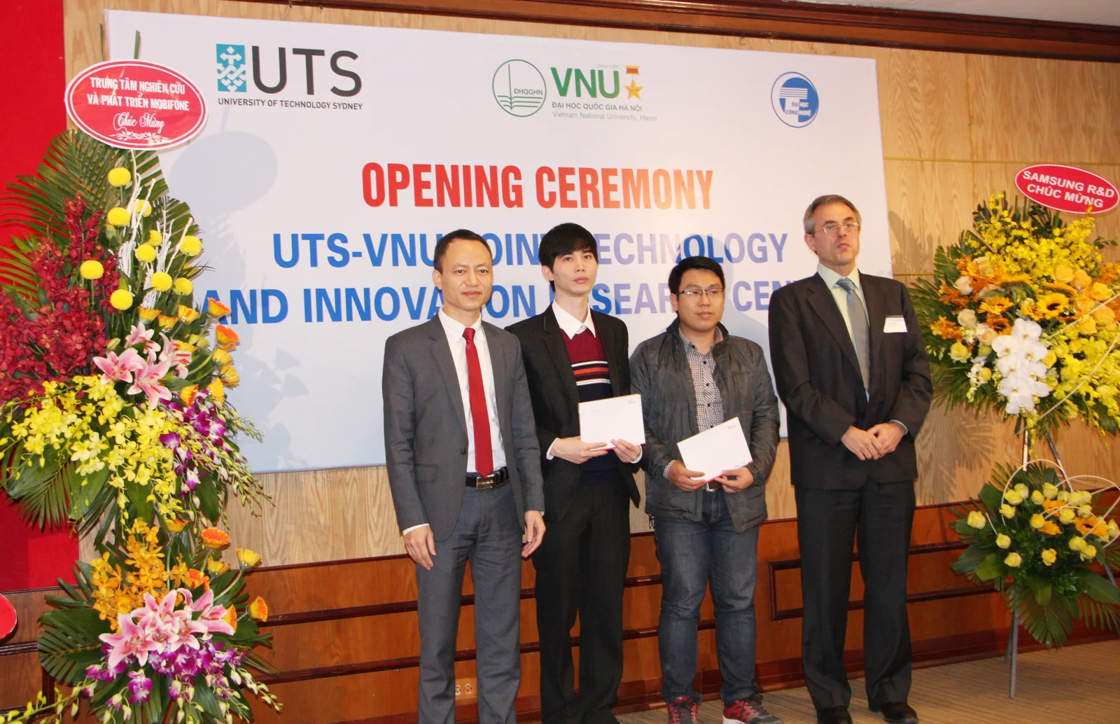 Four participants at the opening ceremony stand before the UTS–VNU Joint Technology and Innovation Research Centre banner.
