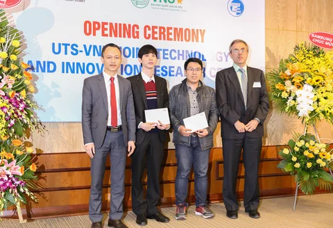 Four participants pose with documents in front of the centre opening banner.