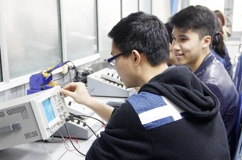 Two students work together at electronic laboratory equipment.